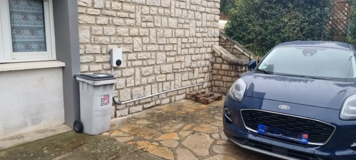 Voiture électrique branchée à une borne installée le long d'un mur en pierre